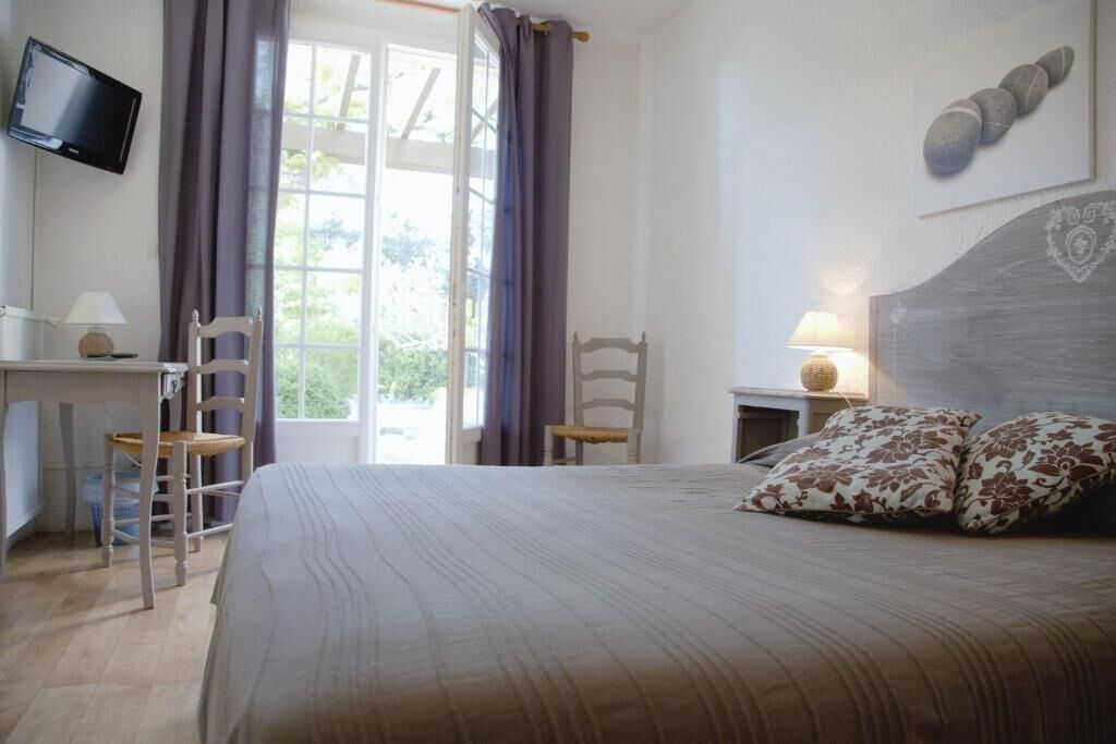 Une chambre à coucher avec un lit, un bureau, une chaise, un téléviseur et une fenêtre avec des rideaux.