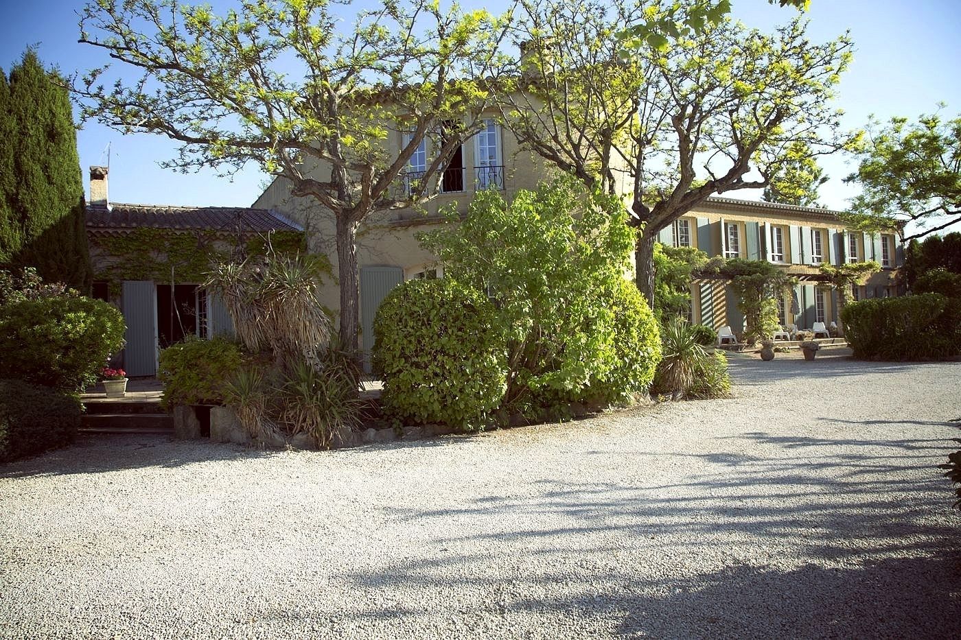 A large, two-story house with a gravel driveway and lush greenery.