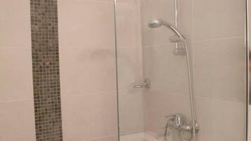 Une douche fermée par des parois de verre, avec un mur carrelé, une douchette à main et un robinet fixé au mur.