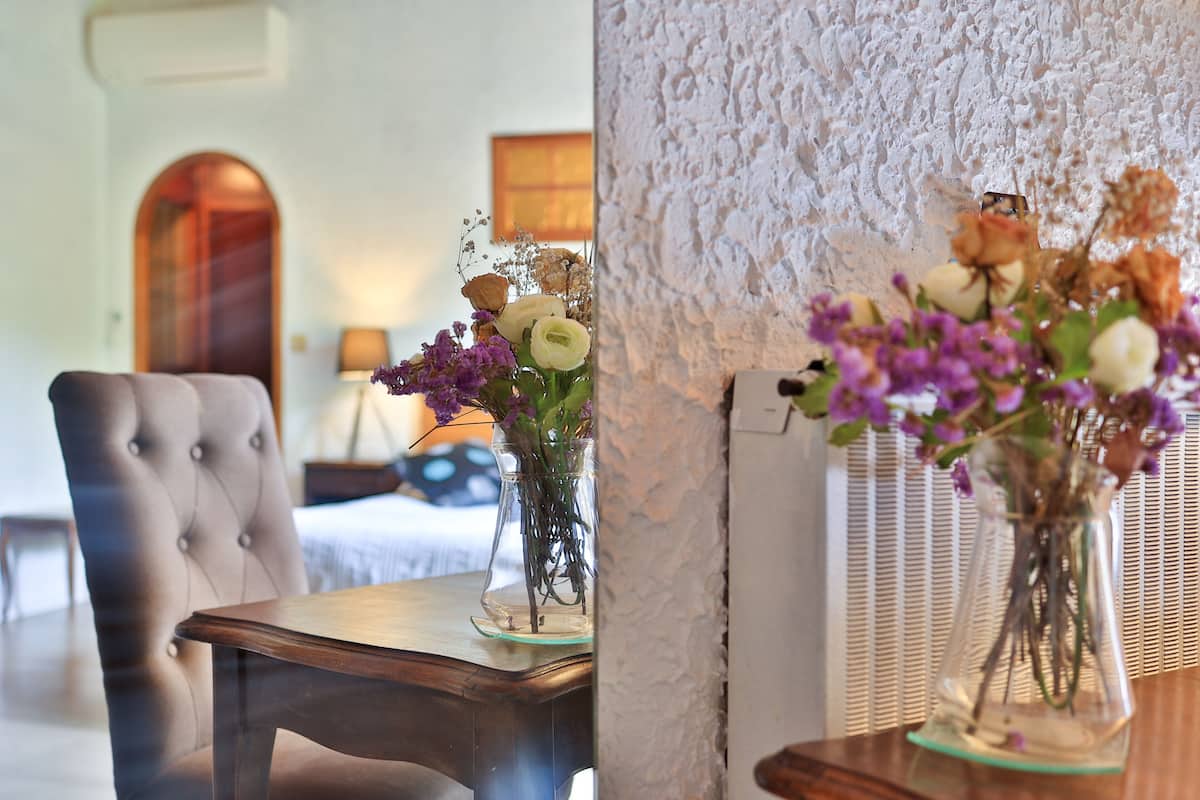 A room with a tufted armchair, a wooden table, and two vases with flowers.