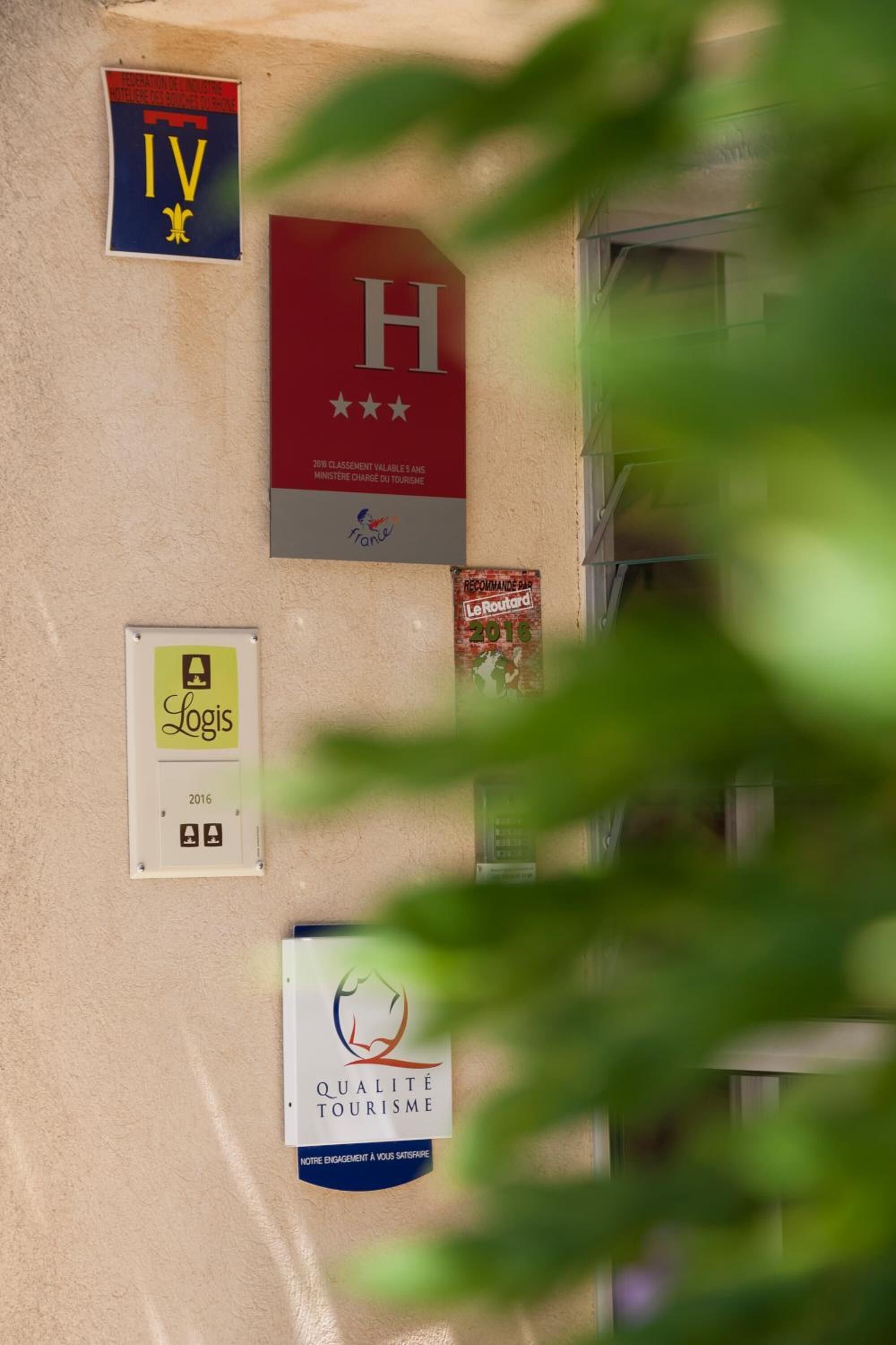A wall with various signs, including a red sign with a white 'H' and stars, a sign with 'Logis' and a year, and a sign with 'Qualité Tourisme'.