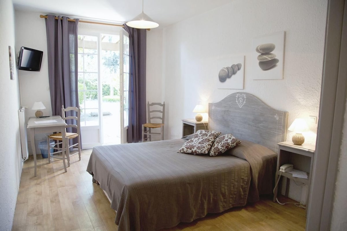 Un dormitorio con cama, mesitas de noche, escritorio, sillas, televisor y una obra de arte en la pared.