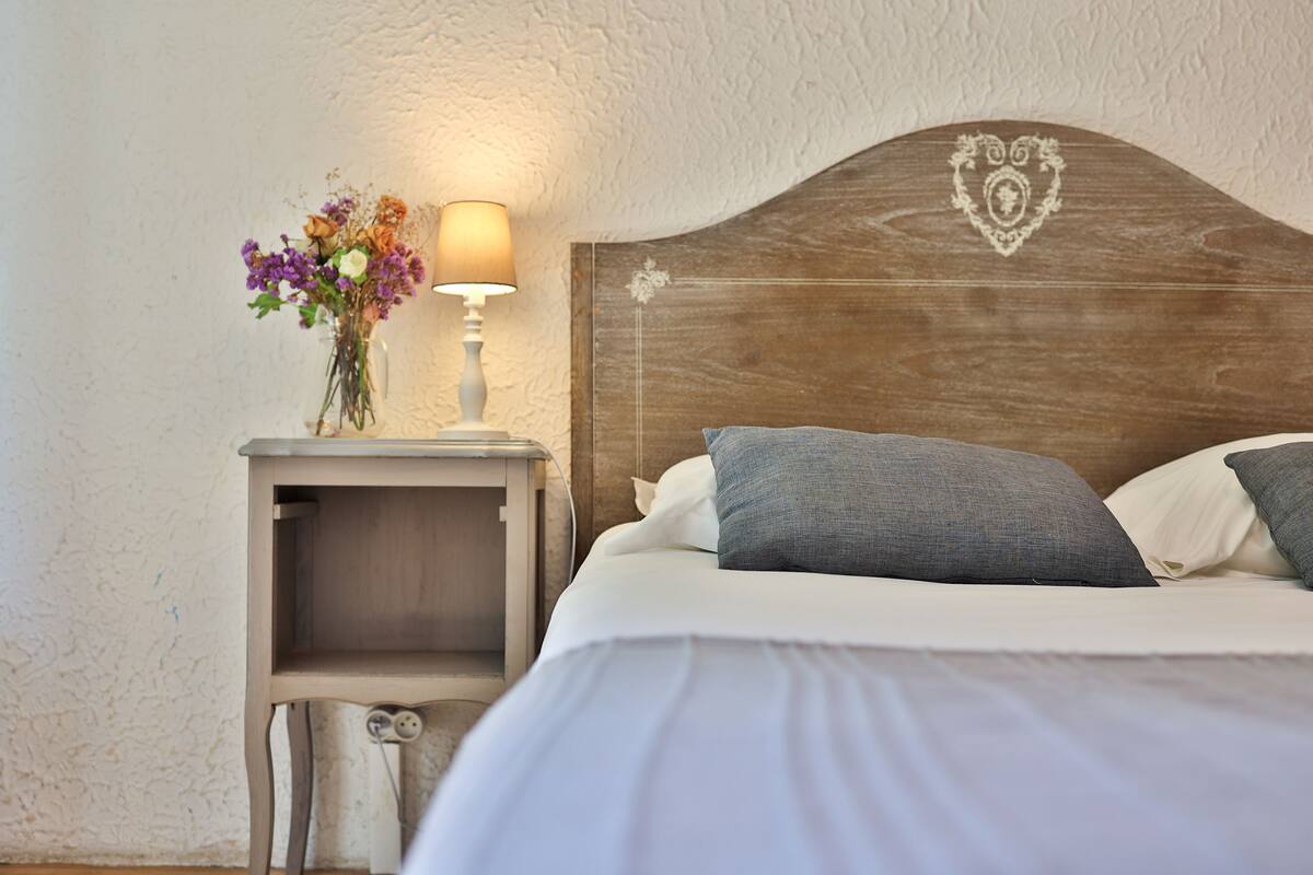 A neatly made bed with a wooden headboard, a bedside table with a lamp, and a vase with flowers.