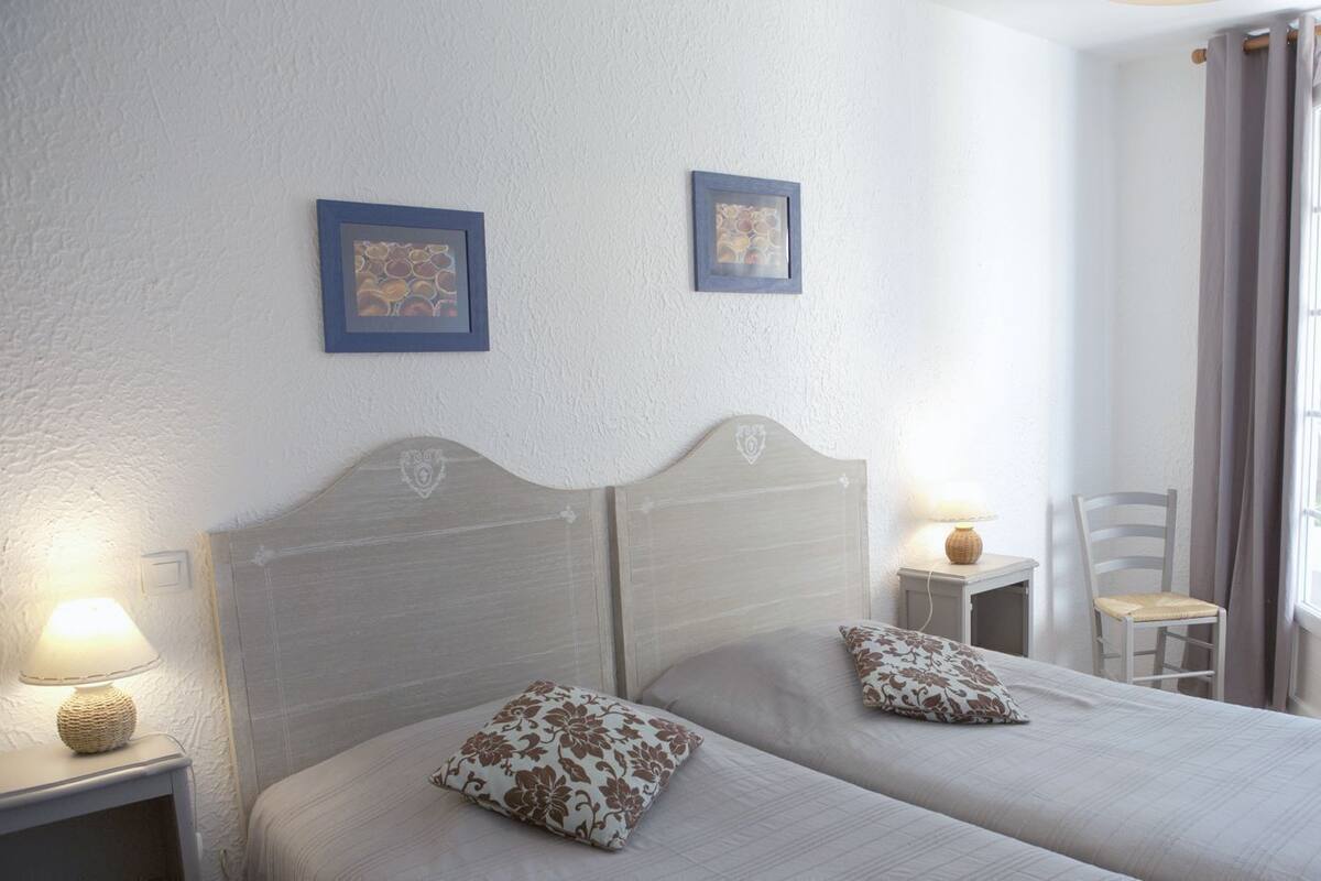A double bed with floral pillows, a nightstand with a lamp, and two framed pictures on the wall.