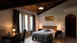 Een slaapkamer met een houten plafond, een bed met een gestreept kussen, twee nachtlampjes, een bureau met een lamp en een stoel.