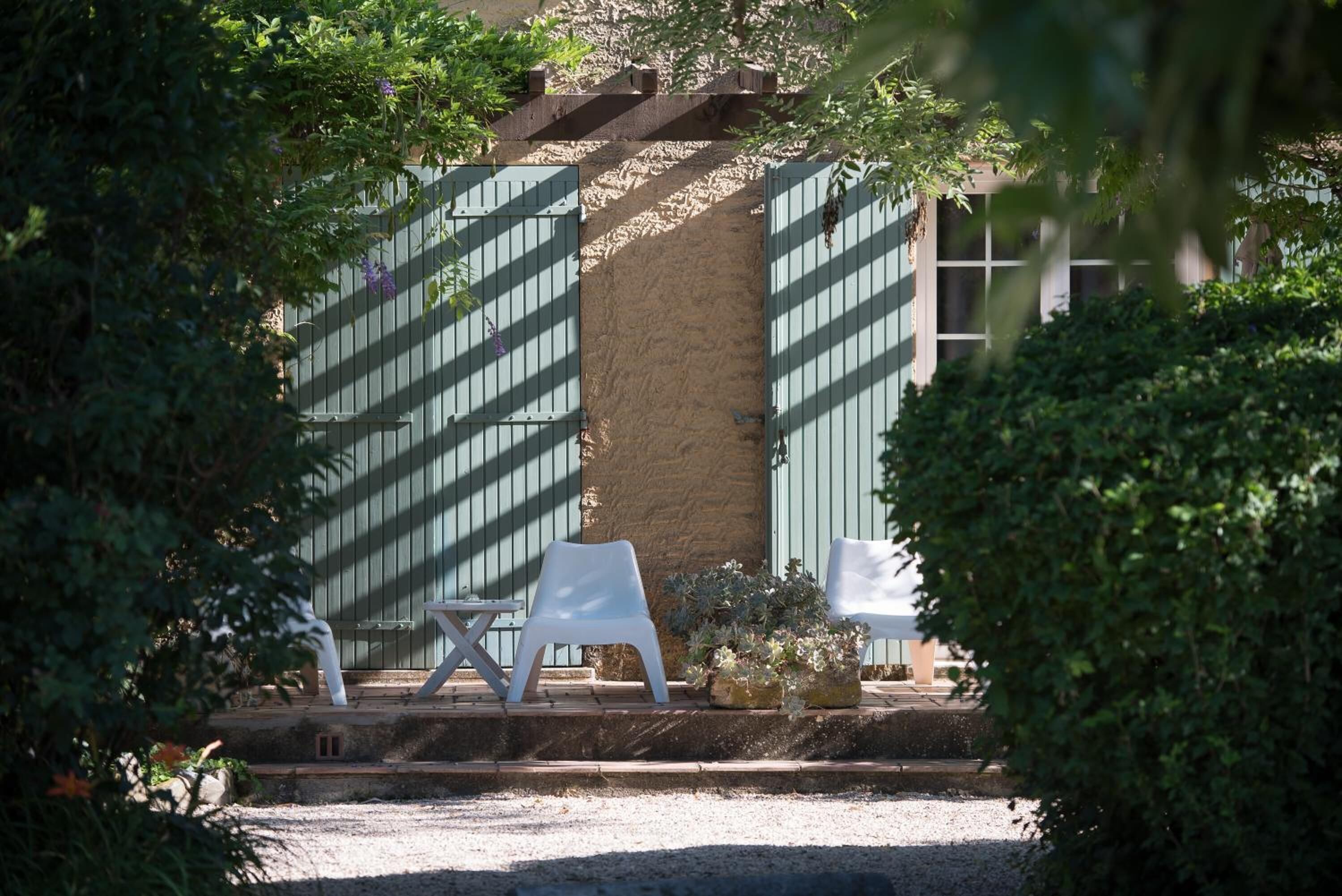 A garden area with a paved walkway, two white chairs, and a small table.