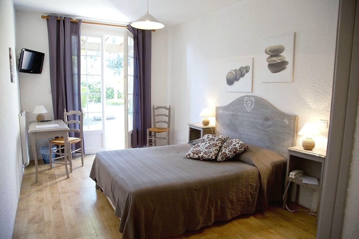 A bedroom with a bed, a desk, a chair, a television, and a window with curtains.