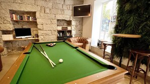 A pool table with a green felt surface, a leather armchair, and a television mounted on a stone wall. - Hôtel Holzer II (Porto-Vecchio)