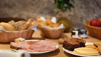 Un buffet de petit-déjeuner proposant une variété d’aliments, notamment du pain, des viennoiseries, du jambon, un gâteau au chocolat et des biscuits.