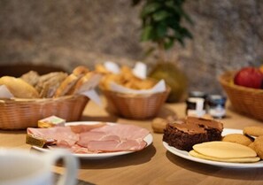 Un bufé de desayuno con diversas opciones de comida, como pan, pasteles, jamón, pastel de chocolate y galletas.
