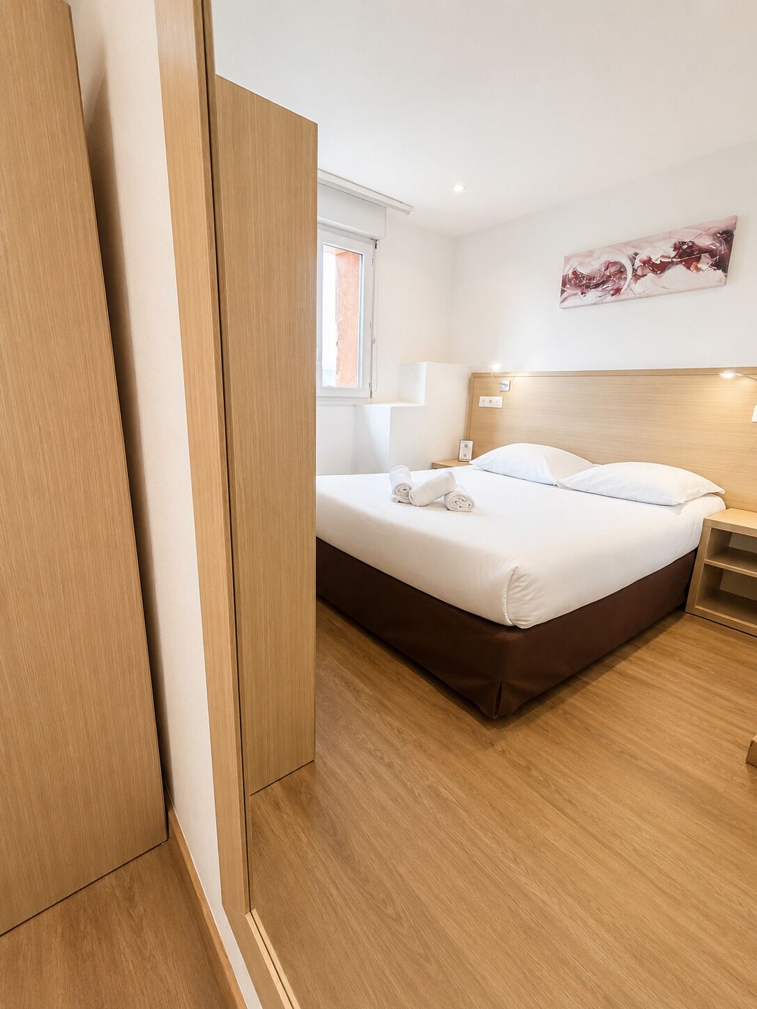 A hotel room with a bed, bedside table, and a painting on the wall.