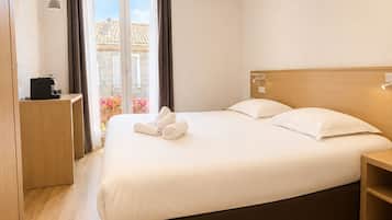 Habitación de hotel con una cama grande, una mesita de noche, un escritorio con cafetera y vistas al exterior.