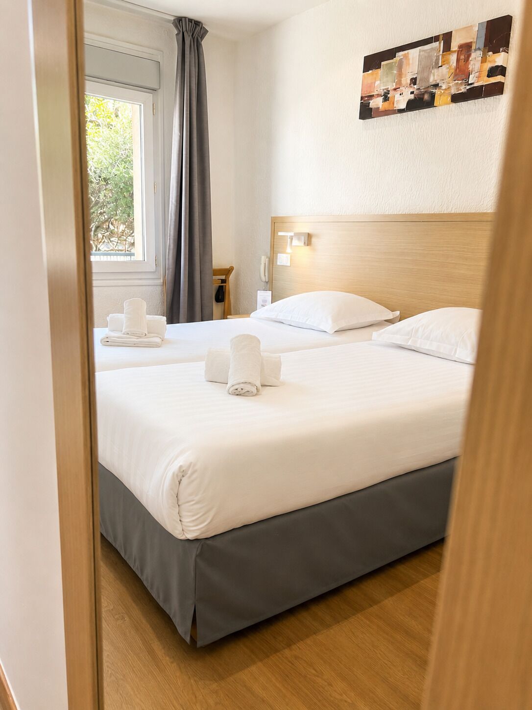 Een hotelkamer met twee bedden, een houten hoofdbord, een nachtkastje met een lamp en een schilderij aan de muur.