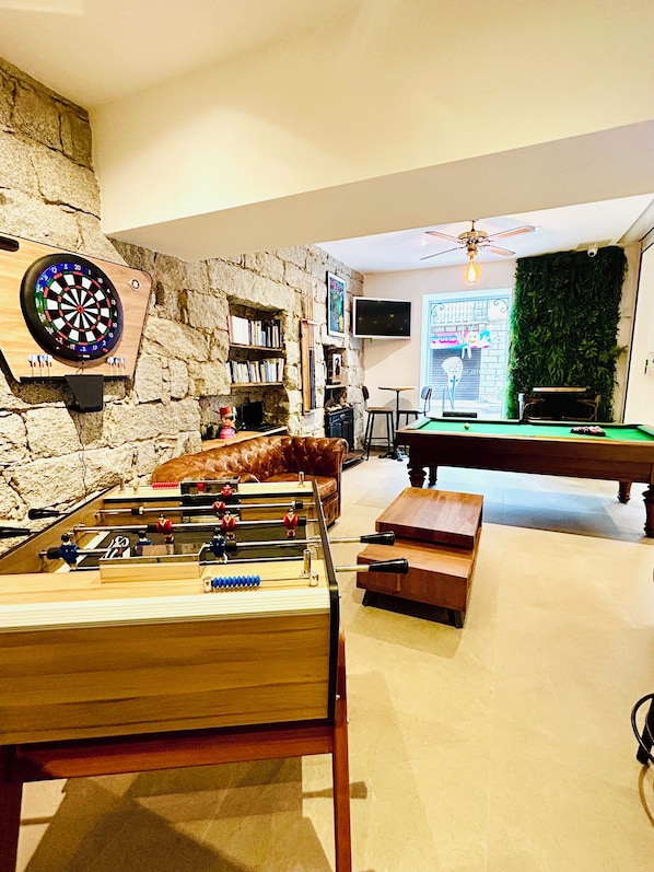 Una habitación con mesa de futbolín, dardos y billar, que presenta paredes de piedra y una pared verde con plantas.