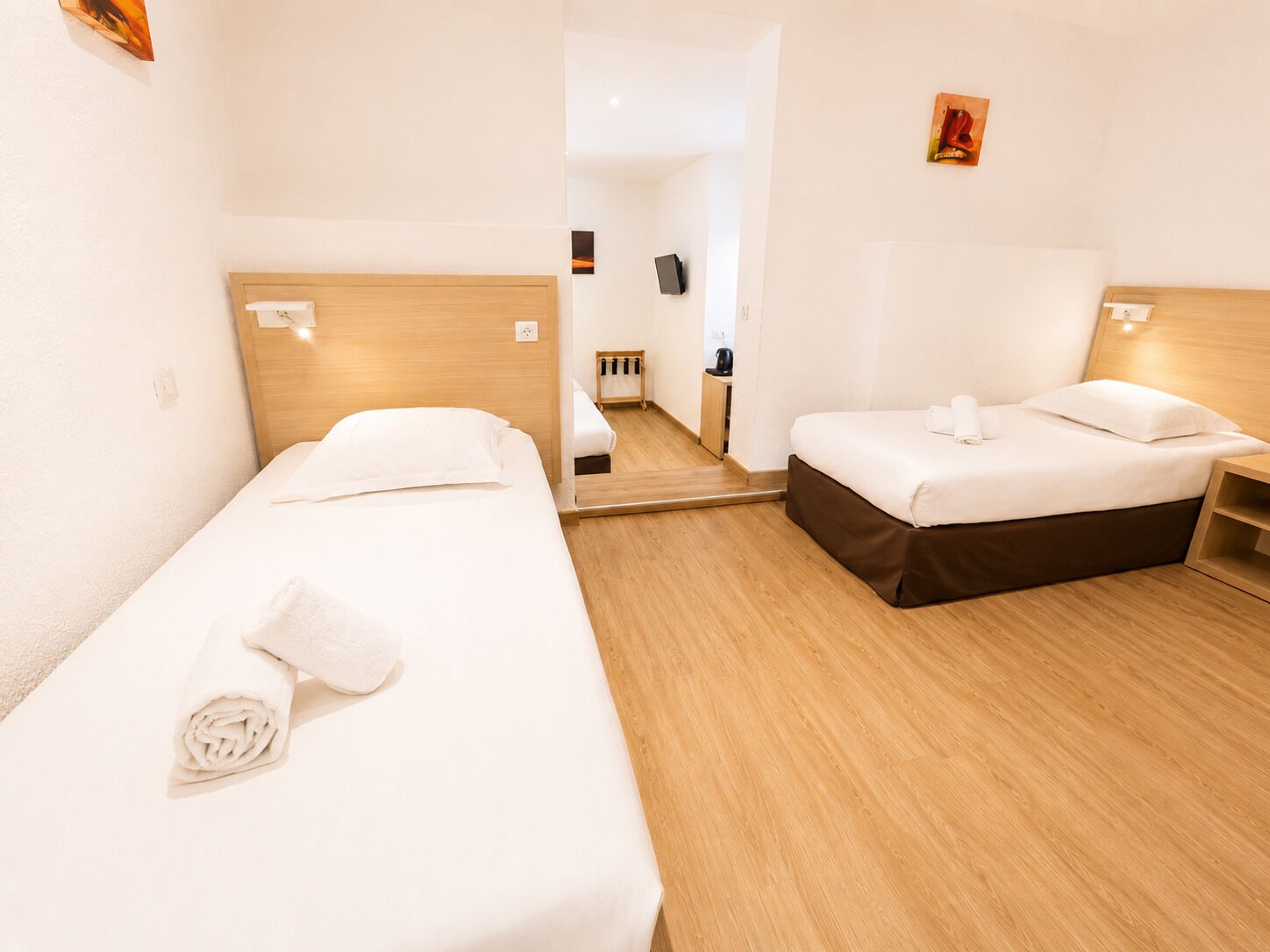 Une chambre d’hôtel avec deux lits simples, un plancher en bois, une petite table de chevet et un miroir.