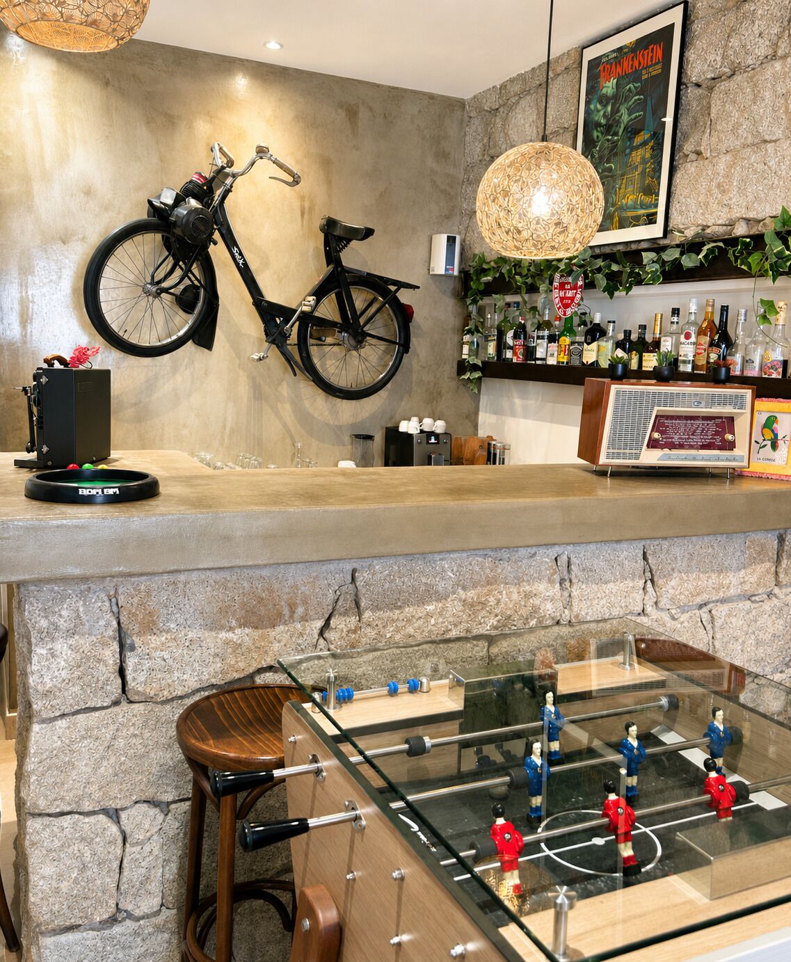 A bar area with a bicycle mounted on the wall, a foosball table, and a shelf with various bottles.