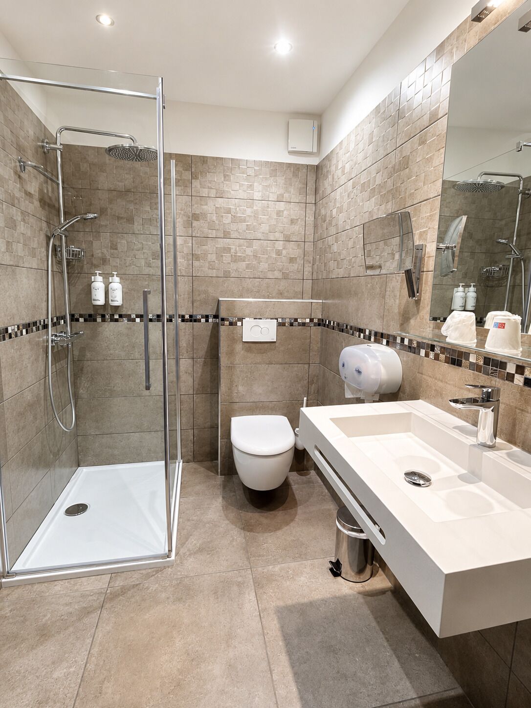 Ein modernes Badezimmer mit einer gläsernen Duschkabine, einer weißen Toilette und einem großen Waschbecken mit Spiegel.