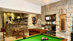 A billiards table with a pool cue and balls, a leather sofa, a dartboard, a bicycle, and a bookshelf with books and a small figurine. - Hôtel Holzer II (Porto-Vecchio)