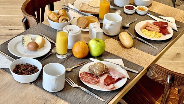 A breakfast table with various food items, utensils, and a chair. - Hôtel Holzer II (Porto-Vecchio)