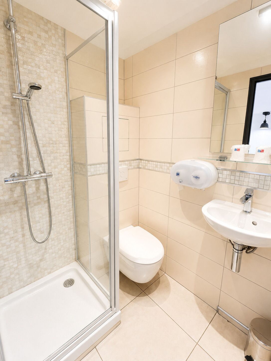 Un baño moderno con cabina de ducha de vidrio, inodoro blanco y lavamanos con espejo.