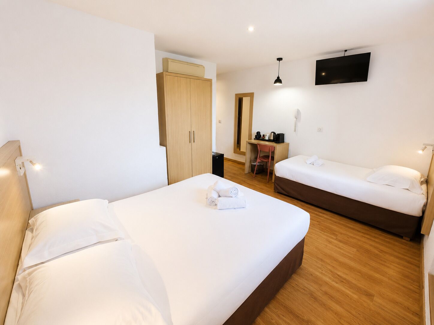 Habitación de hotel con dos camas, un escritorio, una silla, un televisor y un armario.
