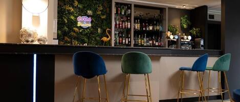 A bar area with a neon sign, a wall of plants, and a shelf of liquor bottles.
