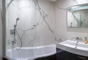 A bathroom with a marble wall, a bathtub, a shower, and a sink with a mirror above it. - Les Tuileries (Fey)