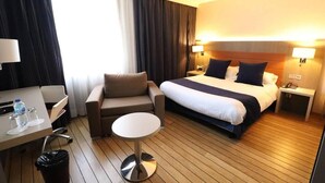 A hotel room with a bed, a desk, a chair, and a small table. - Les Tuileries (Fey)