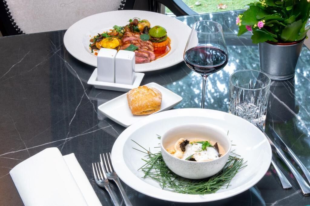 Una mesa de comedor con un plato de comida, una copa de vino tinto y una pequeña maceta.