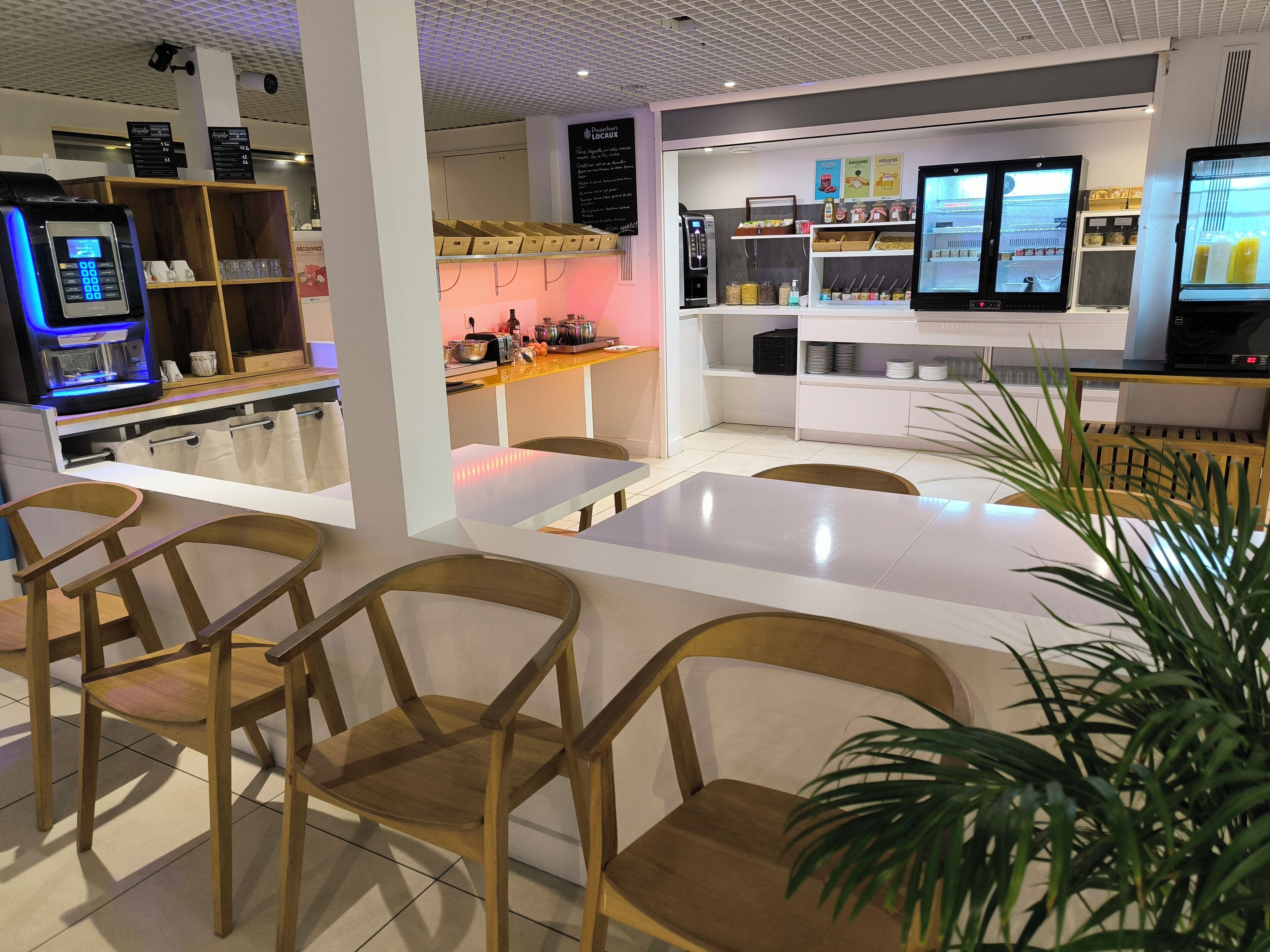 L’intérieur d’un café moderne, avec des chaises en bois, une table blanche et un comptoir où se trouve une machine à café.