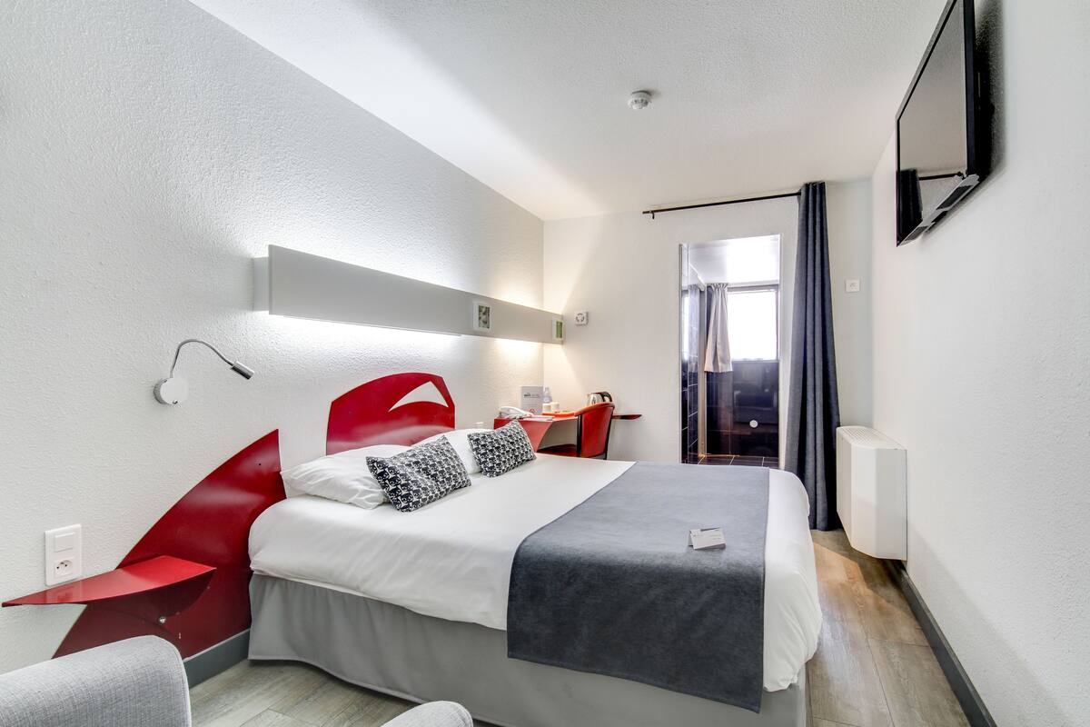 A modern hotel room with a bed, a desk, and a chair.