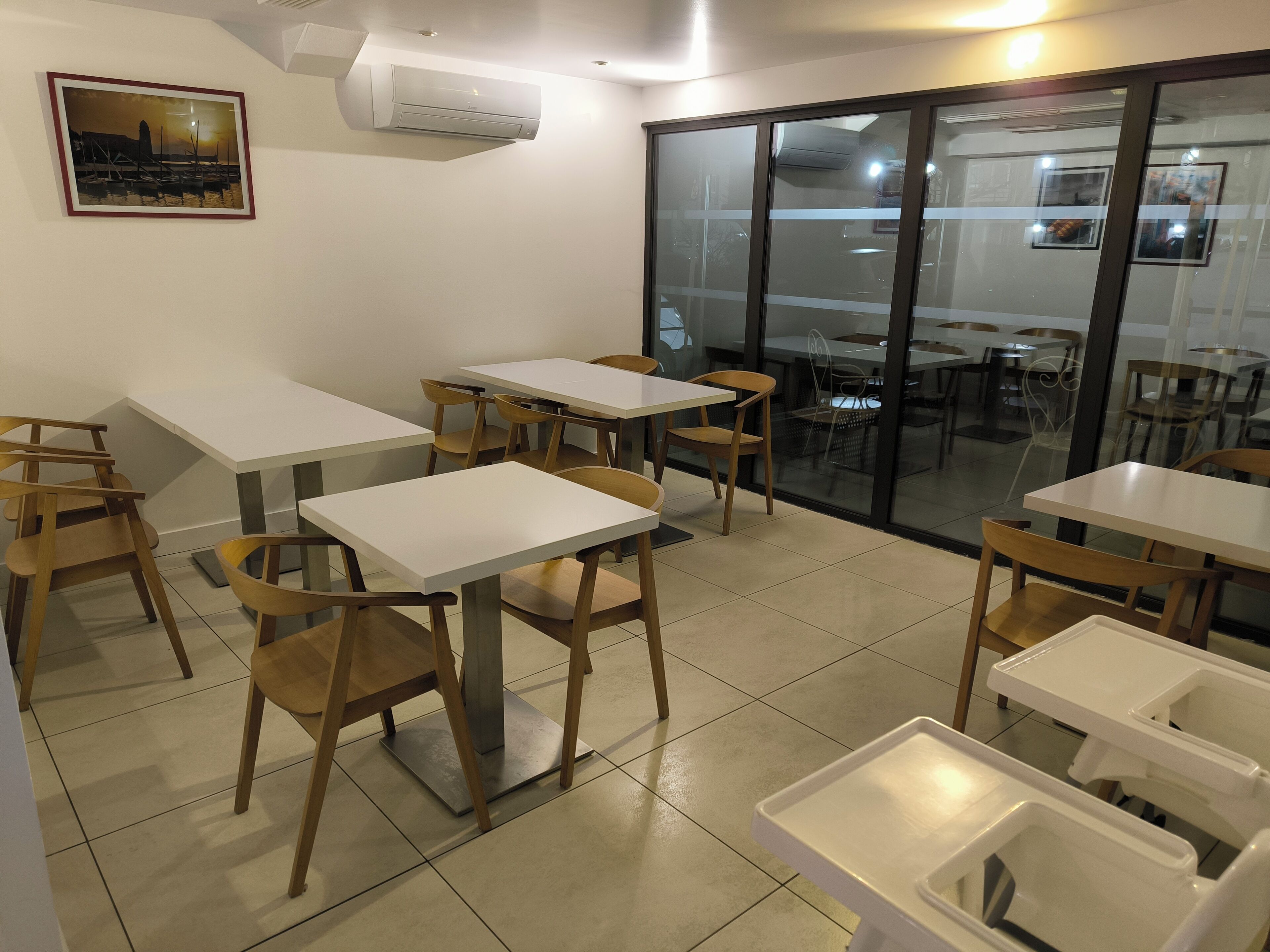 Un espace repas avec des tables et des chaises, un tableau accroché au mur et un appareil de climatisation.