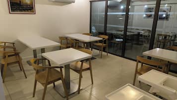 Un espace repas avec des tables et des chaises, un tableau accroché au mur et un appareil de climatisation.