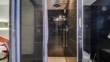 Een moderne badkamer met een glazen douchecabine, donkere betegelde wanden en een wit toilet.