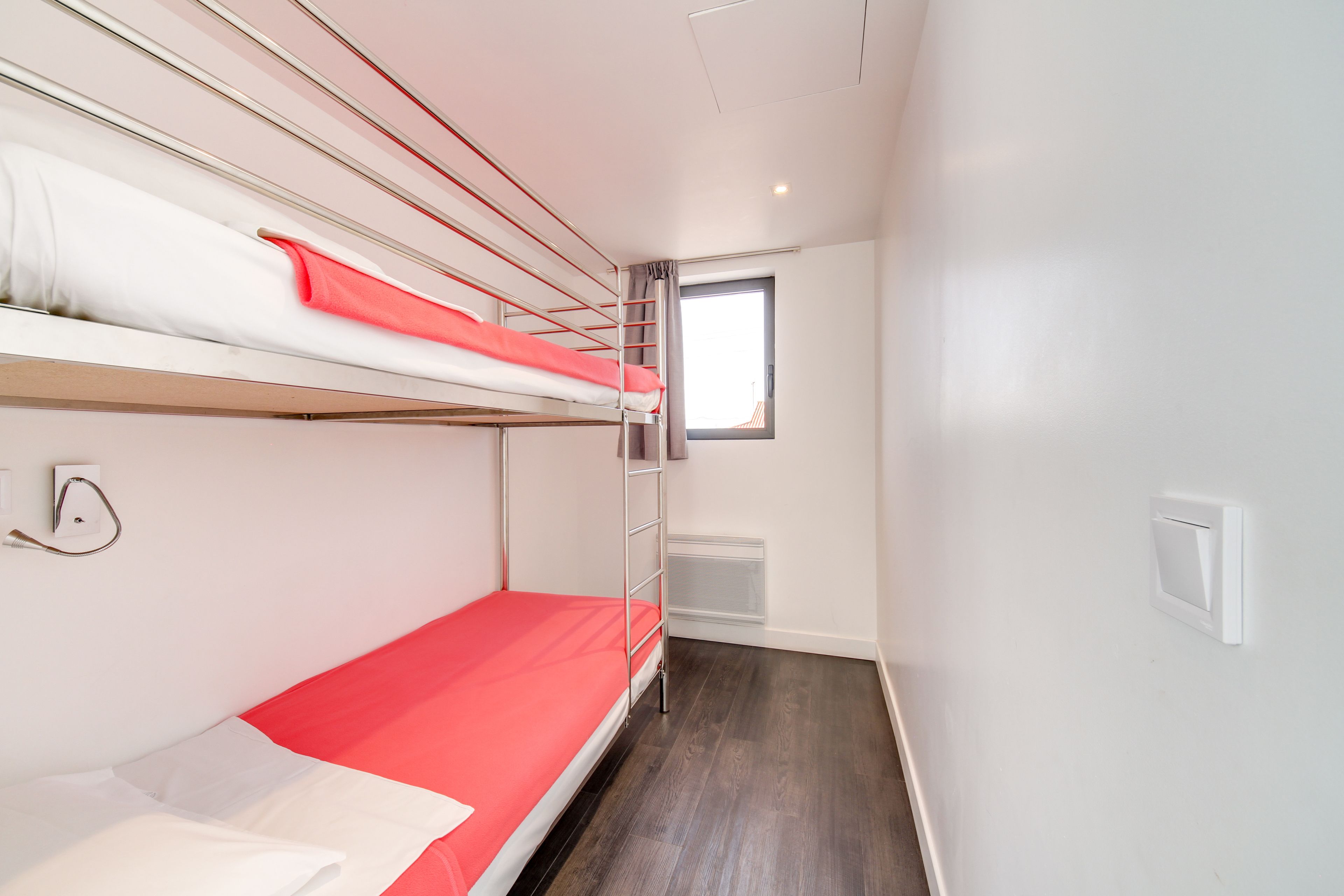 A bunk bed room with a window, a ladder, and a wall socket.