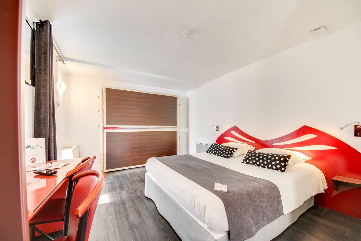 A hotel room with a bed, a desk, and a chair. There is a door and a window.