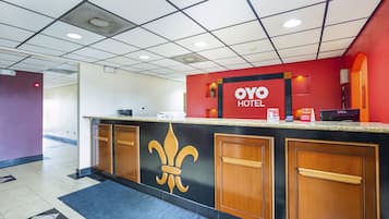 A hotel reception desk with a fleur-de-lis logo, a red wall, and a Dell computer.