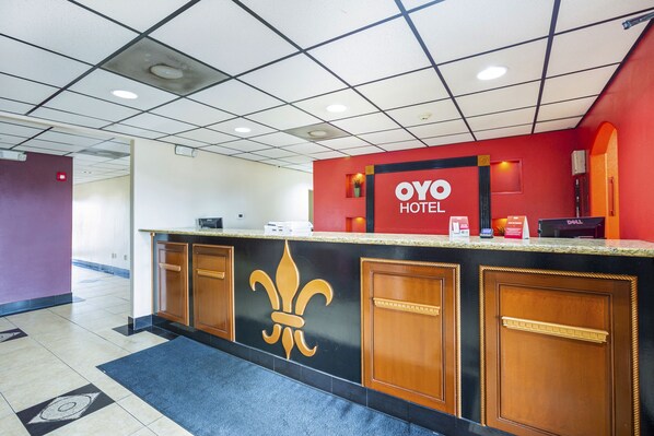 A hotel reception desk with a fleur-de-lis logo, a red wall, and a Dell computer.