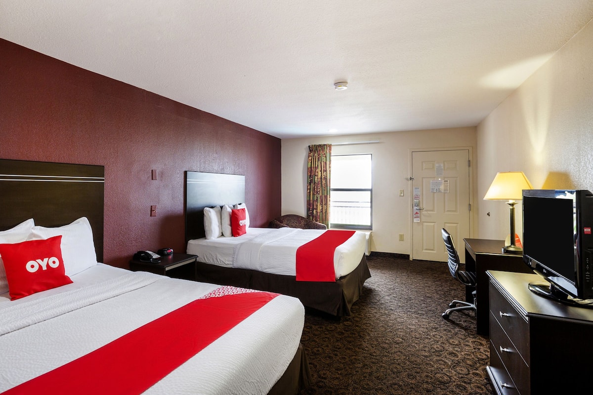 A hotel room with two beds, a desk, a television, and a window with curtains.