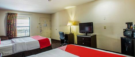 A hotel room with two beds, a television, a desk, and a lamp.