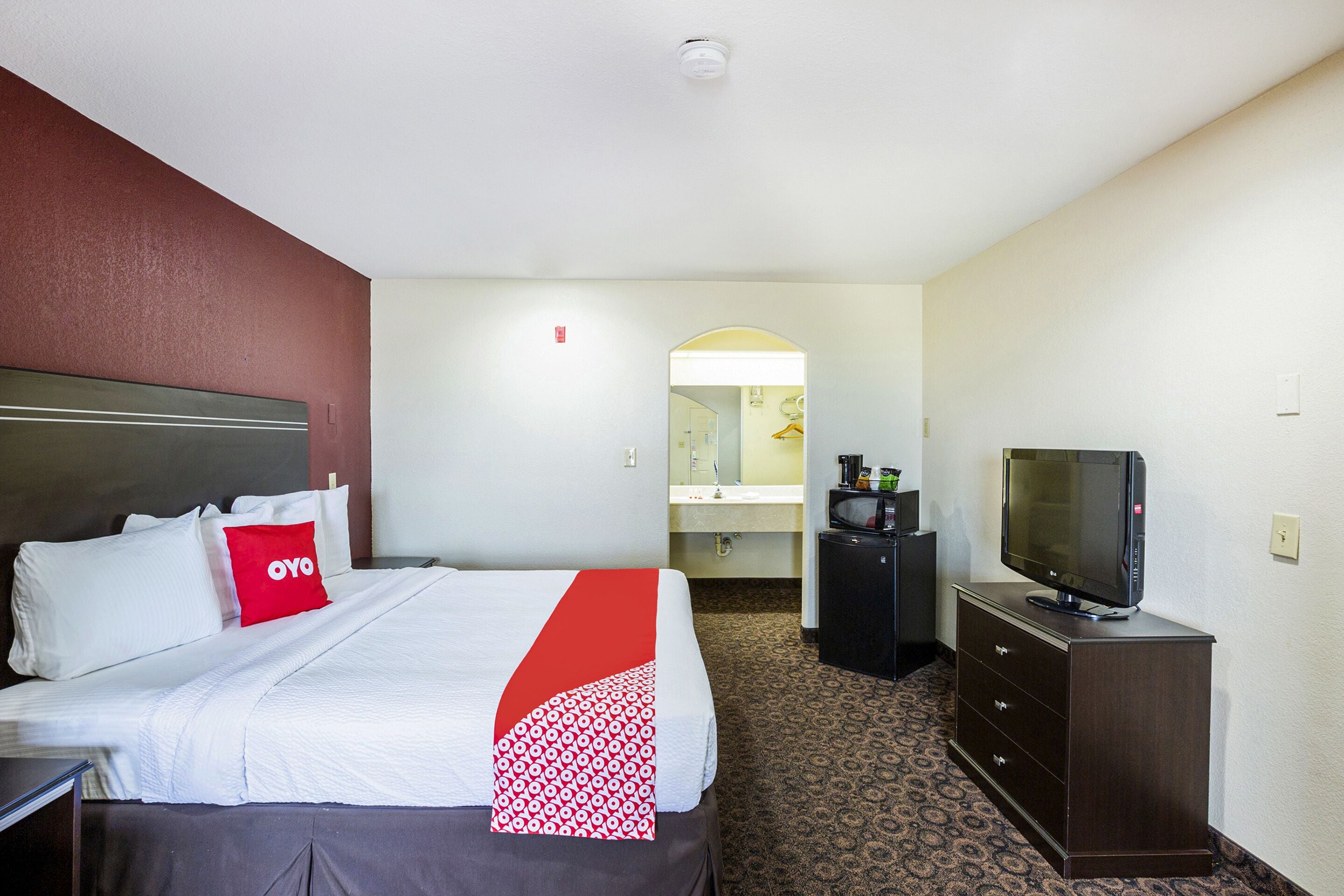 Quarto de hotel com uma cama, televisão, penteadeira e banheiro ao fundo.