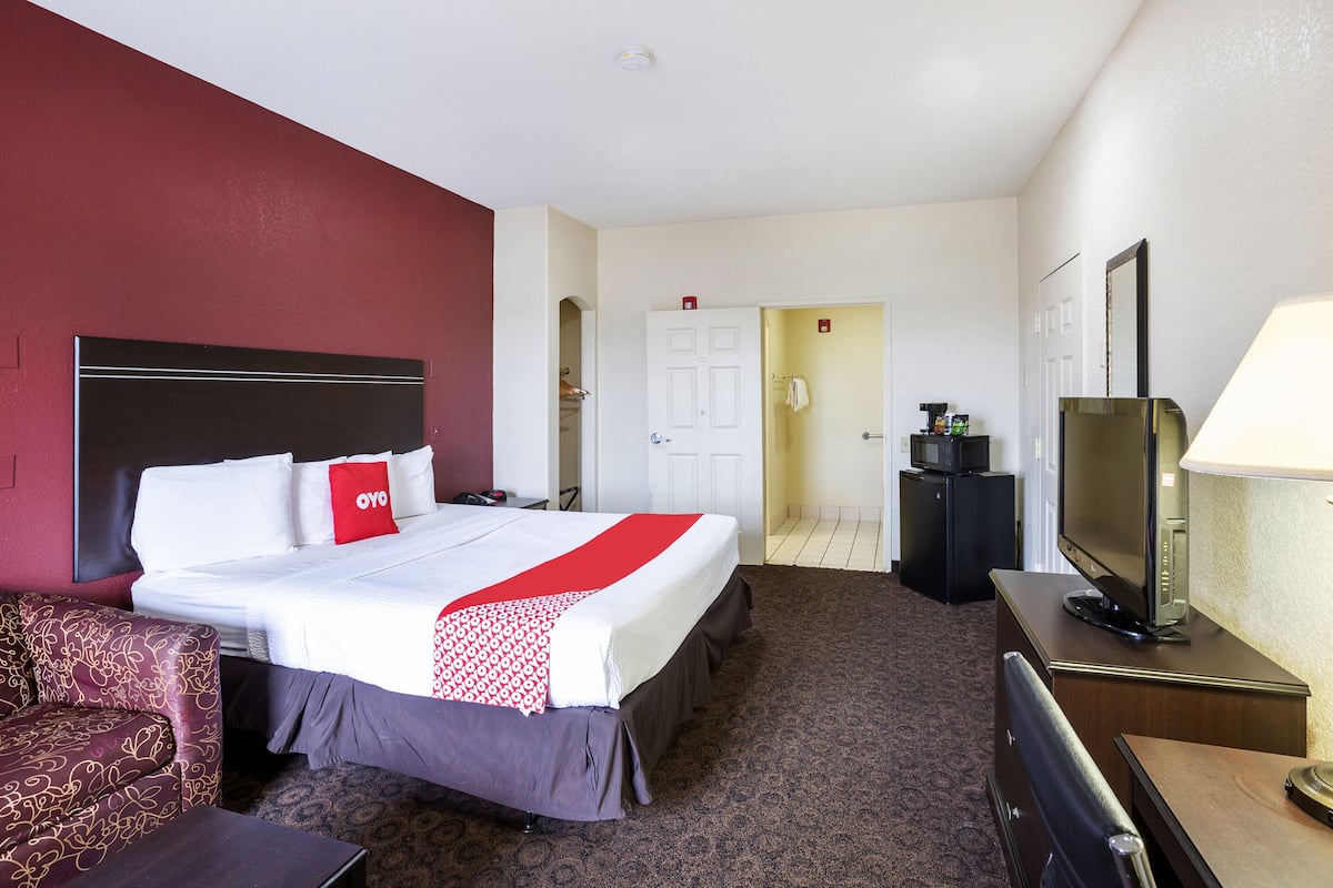 A hotel room with a bed, a desk, a chair, a TV, and a lamp.