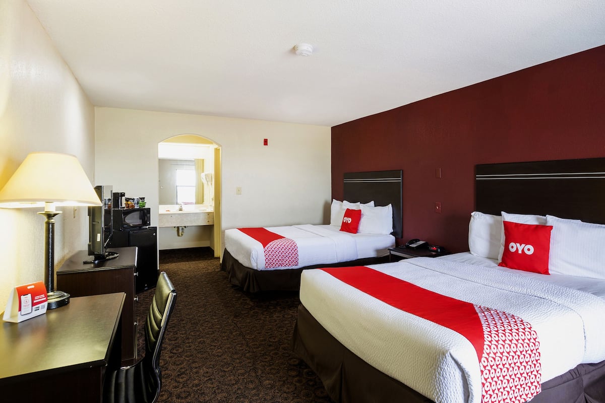 A hotel room with two beds, a desk, a chair, a lamp, a mirror, and a red wall.