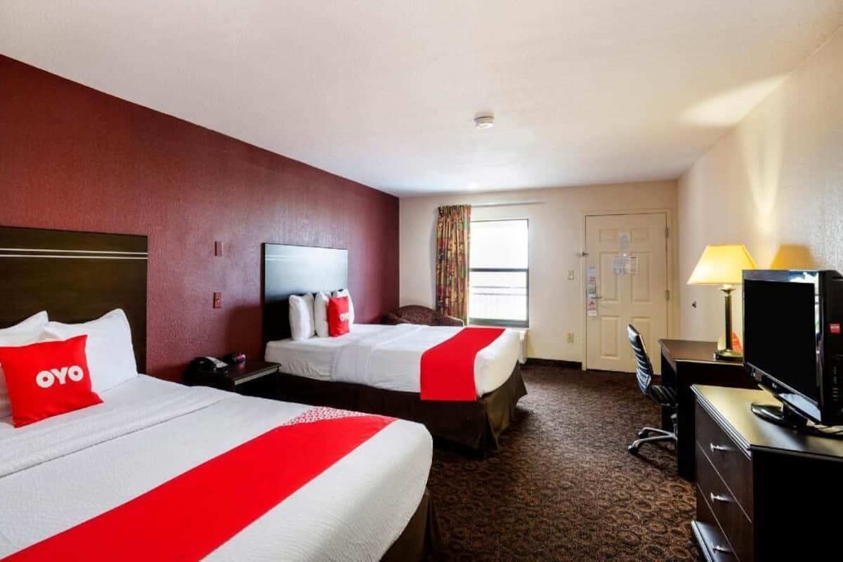 A hotel room with two beds, a desk, a TV, and a window with curtains.