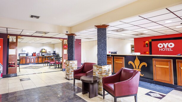 A hotel lobby with a reception desk, seating area, and a kitchen in the background. - OYO Hotel LSU (Port Allen)
