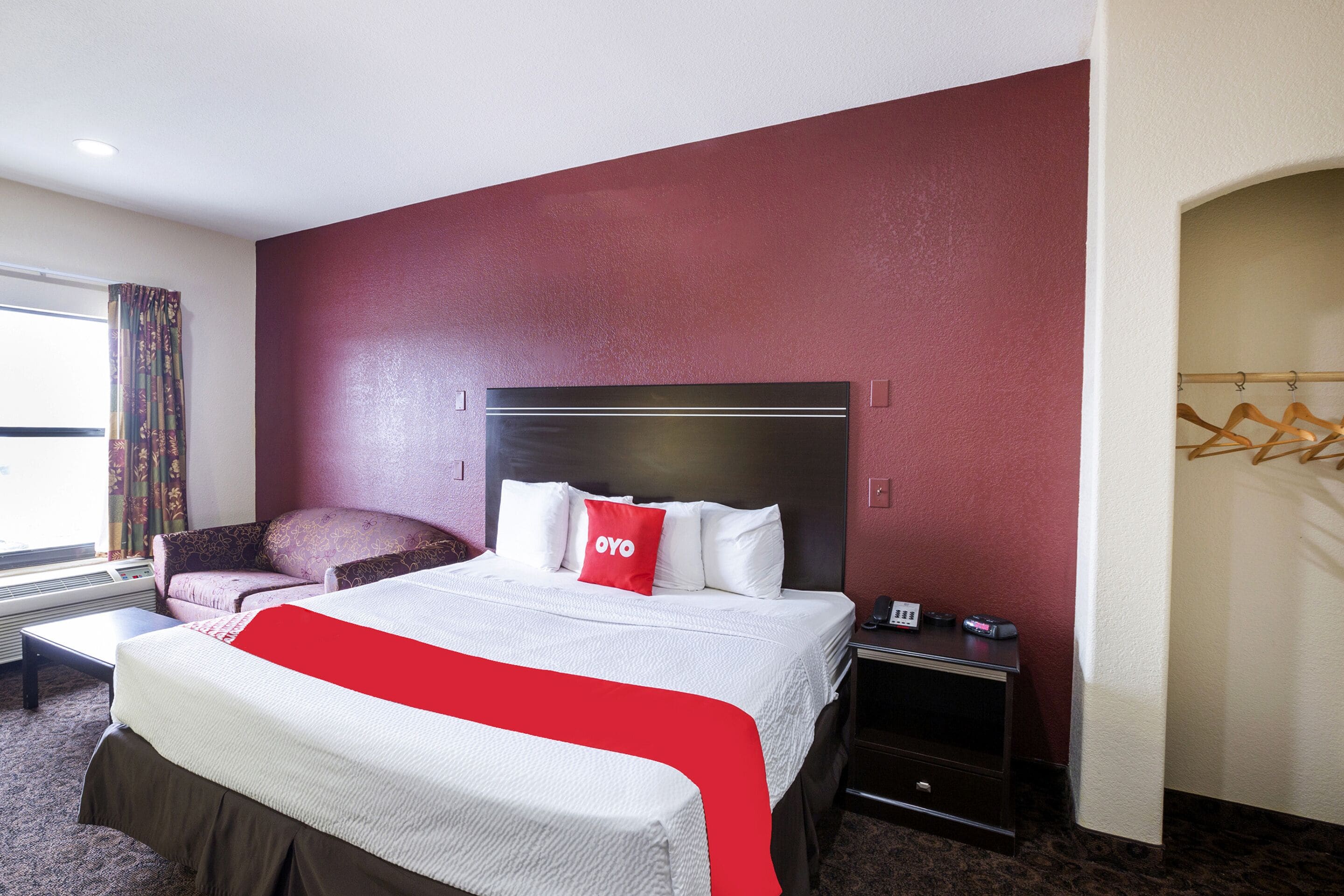 A hotel room with a bed, a chair, a bedside table with a phone, and a window with curtains.