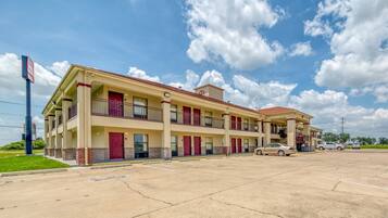 A multi-story motel with a red and beige facade, multiple balconies, and a parking lot.