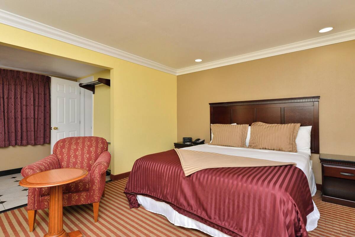 Een hotelkamer met een bed, een stoel, een klein tafeltje en een nachtkastje.