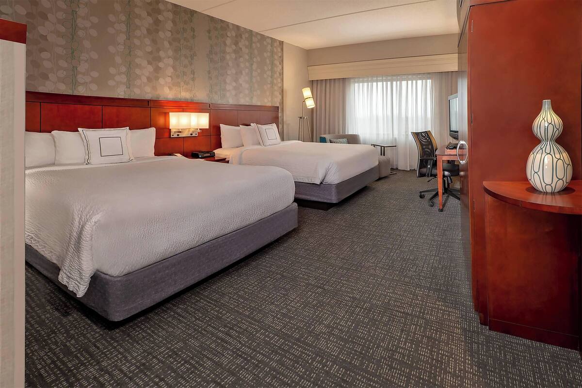 A hotel room with two beds, a desk, a chair, a lamp, and a decorative vase.