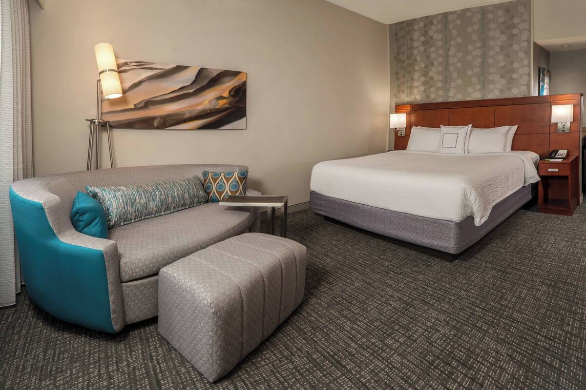 A hotel room with a bed, a sofa, a small table, and a lamp.